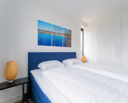 schlafzimmer mit blauem bett und bettzeug, bild mit see über dem Bett